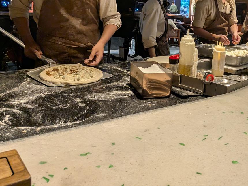 オープンキッチンのカウンターで、焼く前のピザを扱う店の人の手元